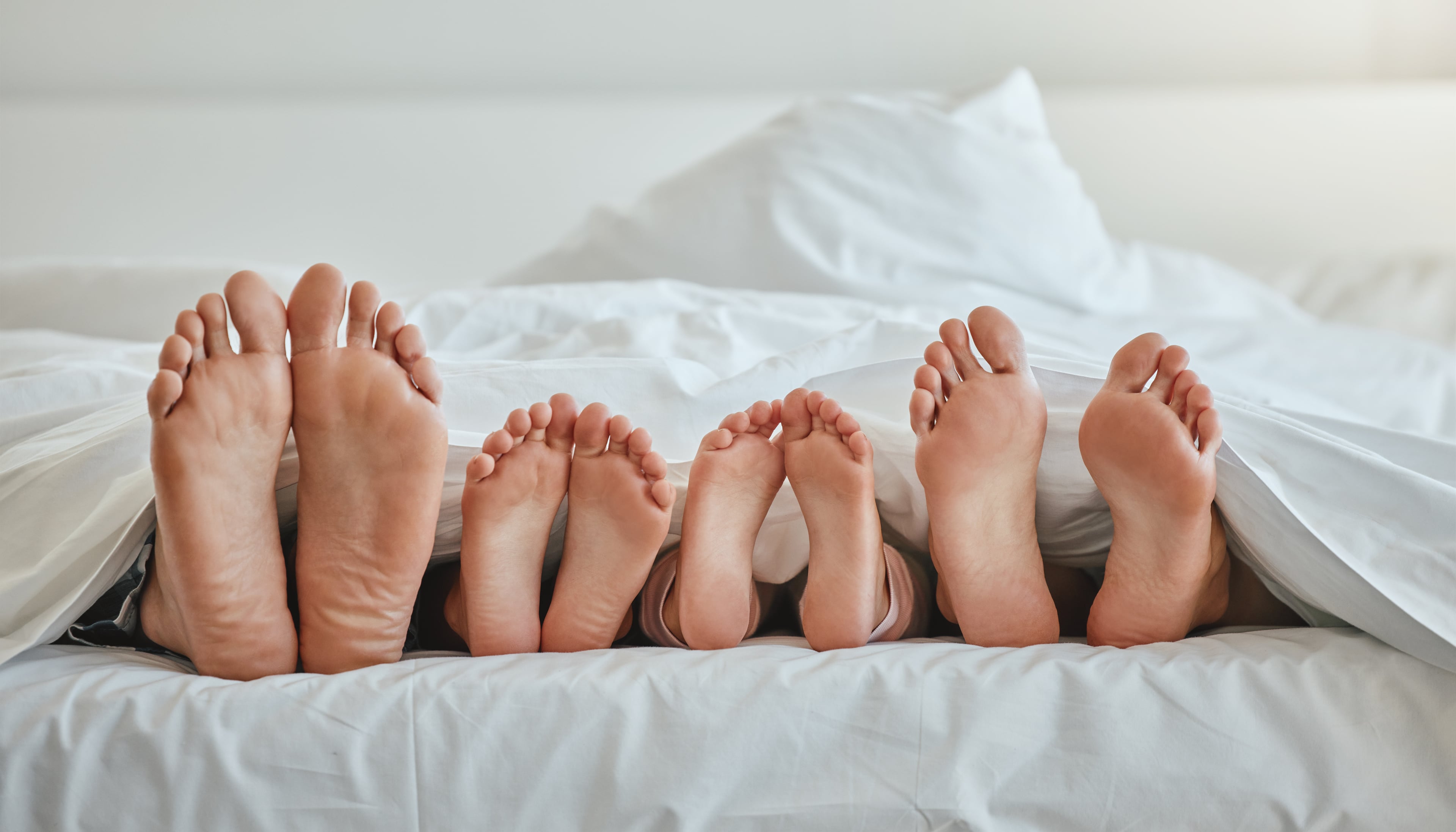 A playful shot of the feet of a family of four poking out of the end of a duvet as they lay bed